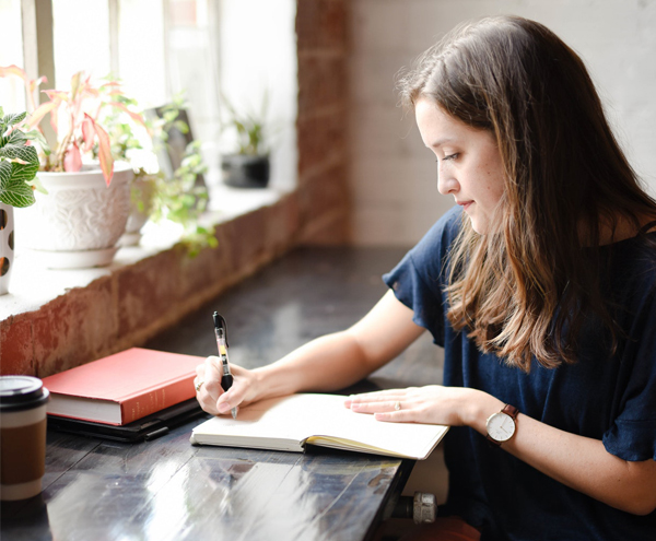 How To Do A Wedding Budget Right Wedding Budget - Woman Writing In A Notebook In Coffee Shop