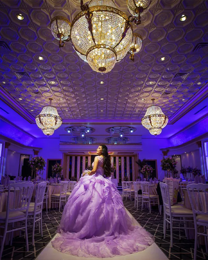 Young woman in a purple ball gown celebrating her quinceanera under elegant chandeliers at a luxurious