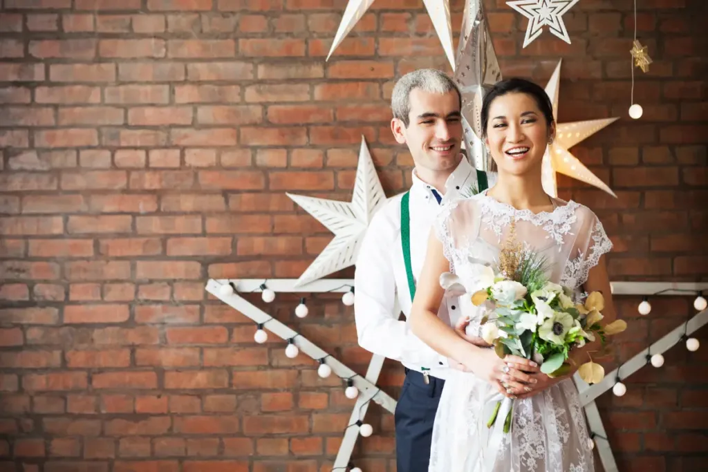 Wedding Aesthetic: How to Choose a Style That Shapes the Entire Experience Couple posing with a bouquet against a brick wall, highlighting a modern wedding aesthetic with warm lighting and minimalist décor